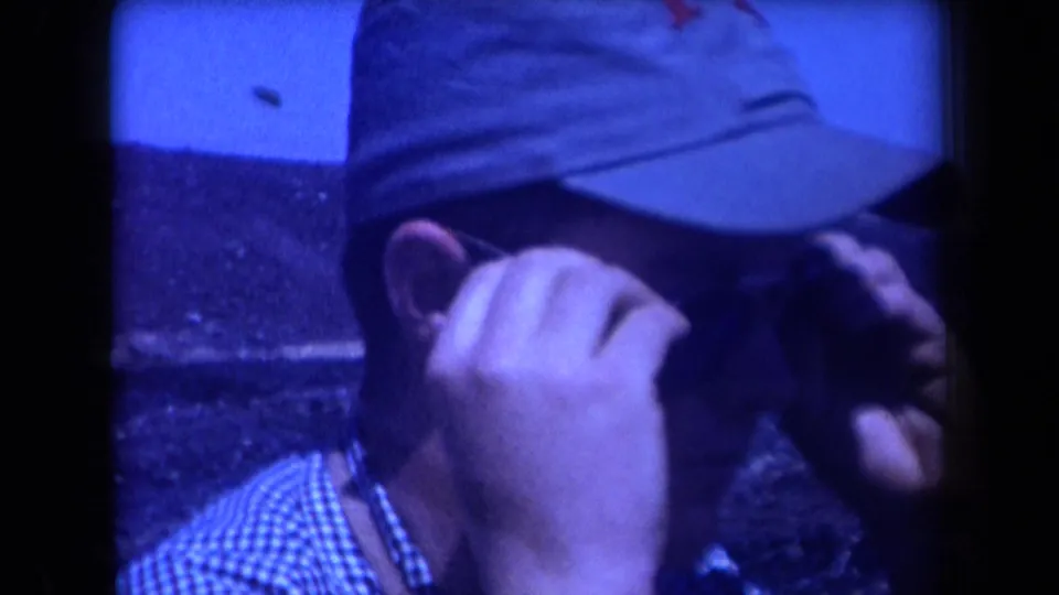 In 1958 Arizona home-movie footage, a capped man in a checkered shirt adjusts his glasses beside a dark coal mound.