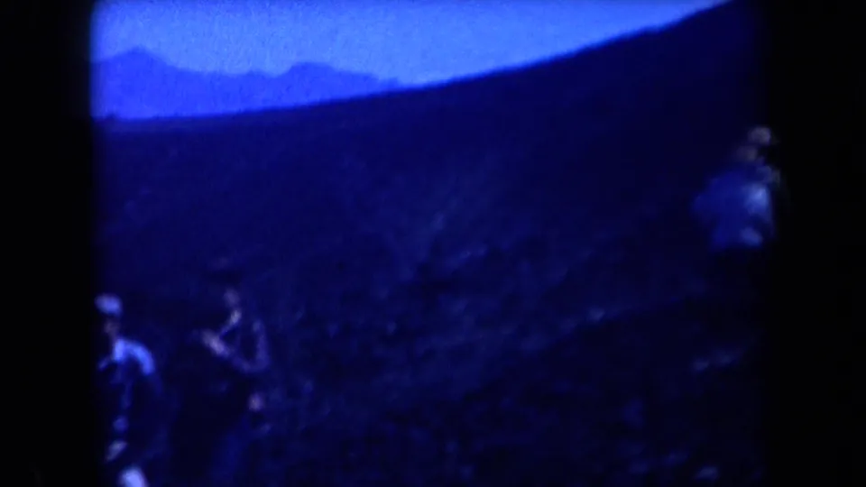 1958 Arizona home-movie frame showing people on a shadowed hillside with distant ridges and a strong blue film cast.