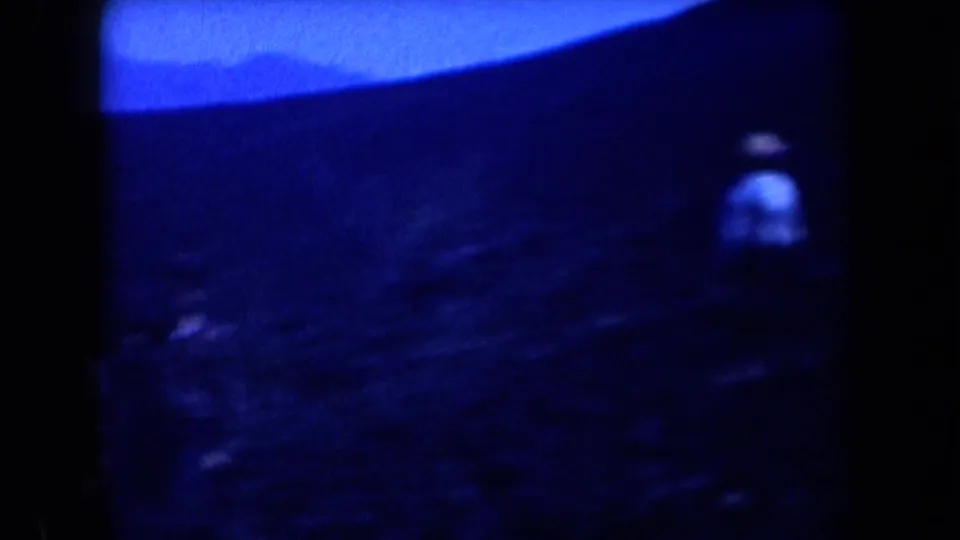 Blue-tinted 1958 Arizona 8mm frame with a distant man crossing a dark, barren mountain slope under bright sky.