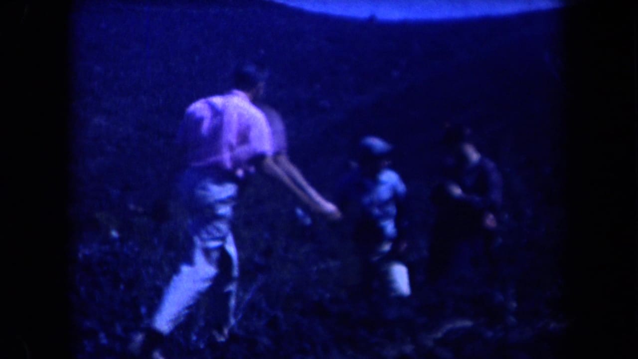 Several men walk and crouch on a dark rocky hillside.