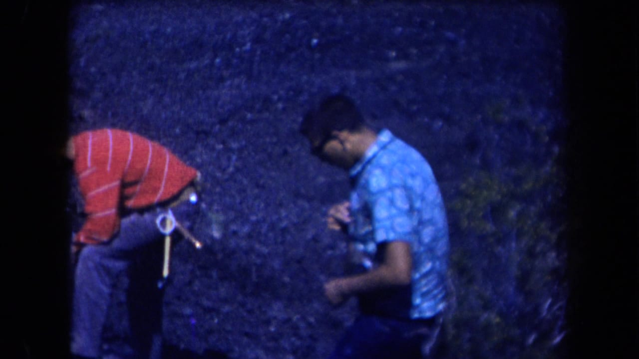 In 1958 Arizona 8mm footage, two adult men in patterned shirts stand on rocky terrain under a strong blue color cast.
