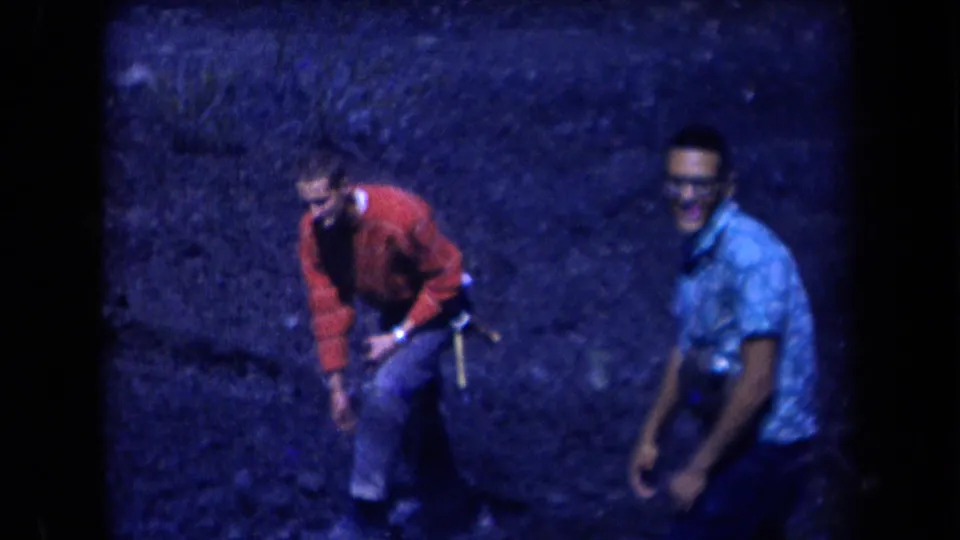 In the 1958 Arizona home movie, the men look back toward the camera while standing on rocky ground in soft blue exposure.