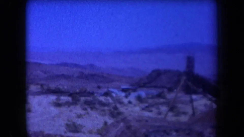 1958 Arizona 8mm frame showing a wide desert mining landscape with low brush, hills, and a distant structure.