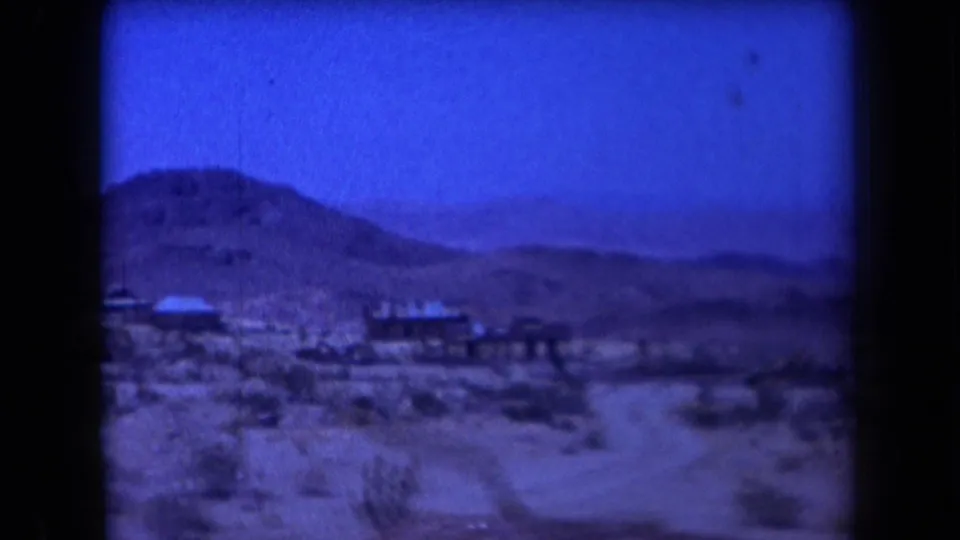 1958 Arizona desert mining site with low structures or equipment set against rounded hills and blue sky.