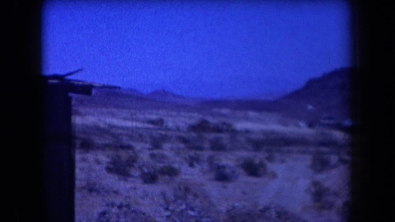 1958 Arizona home-movie frame with open desert, distant hills, scrub, and a dark vertical edge from the film scan.