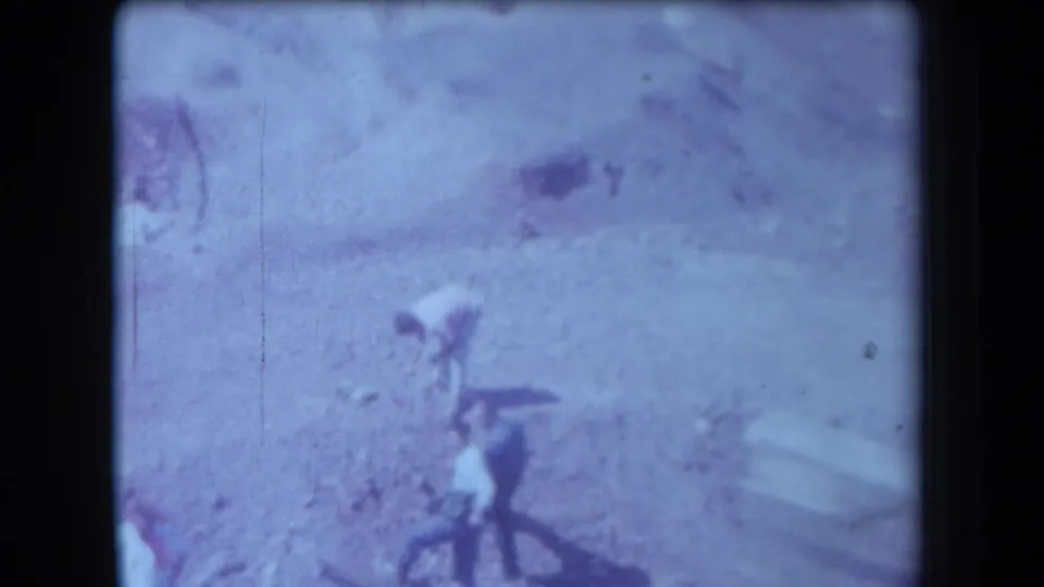 1958 Arizona 8mm frame showing several blurred people bending or standing on sandy desert ground.