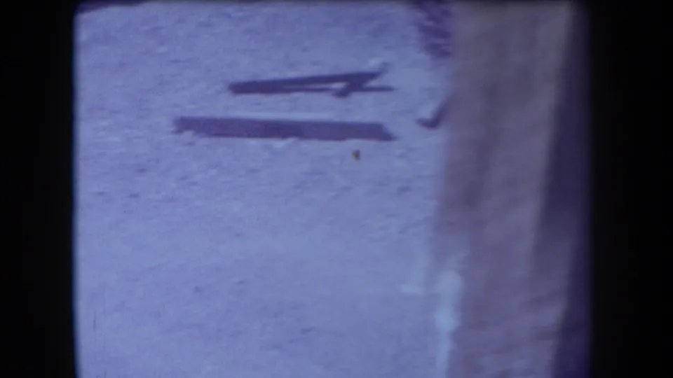 1958 Arizona 8mm frame showing bright sandy ground, long shadows, and indistinct objects or marks near the film edge.