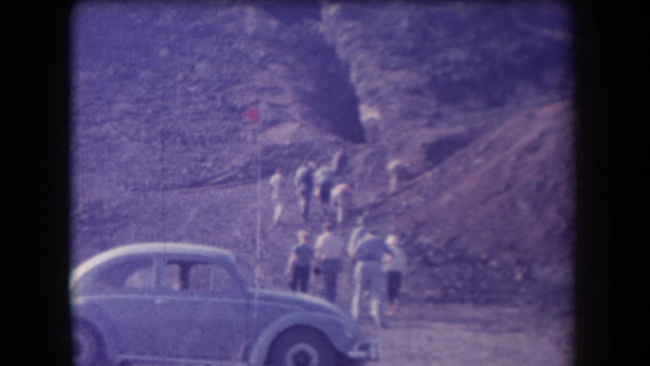Arizona 1958 home-movie frame showing several people hiking on a rocky slope with a light blue rounded car parked in the foreground.