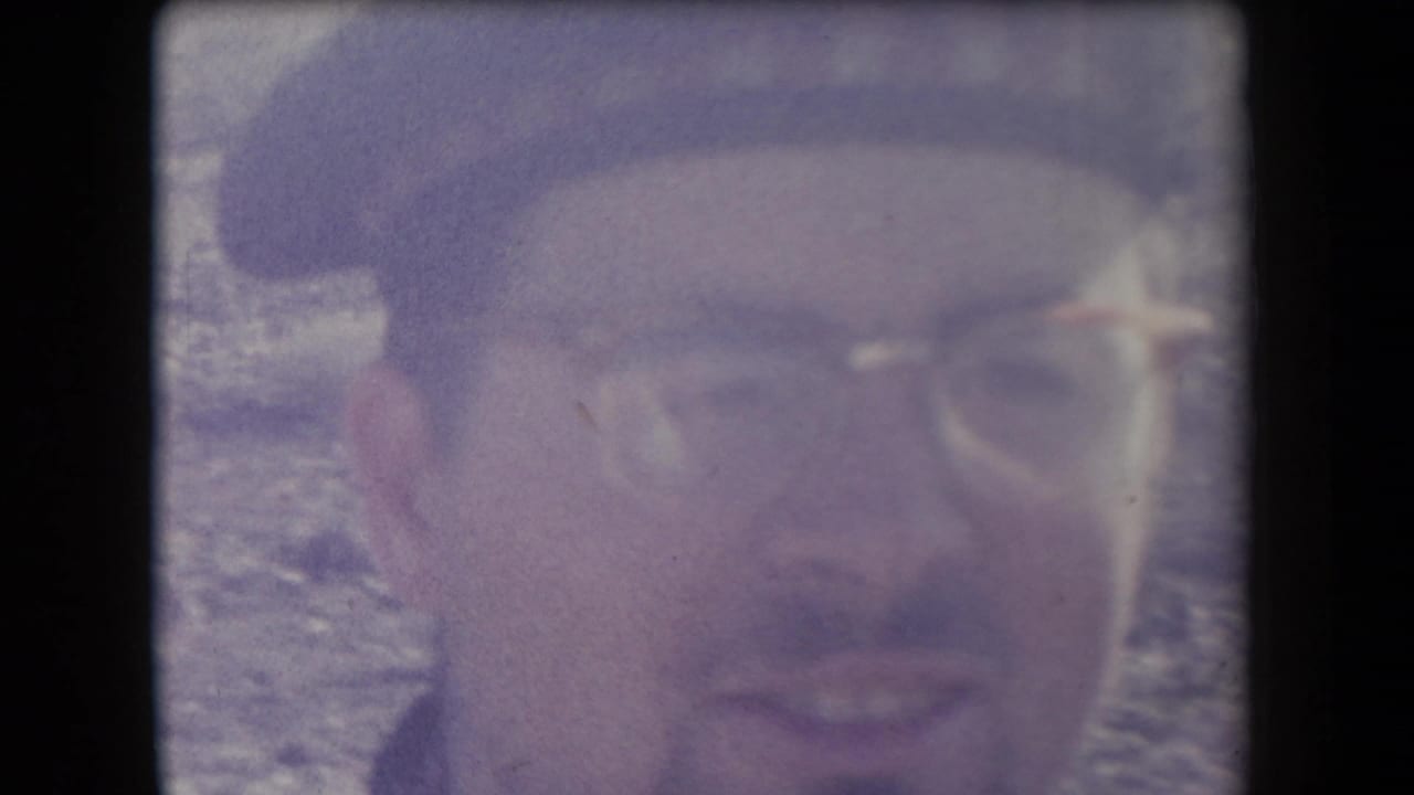 Close-up of a smiling man wearing a hat and glasses in bright desert light.