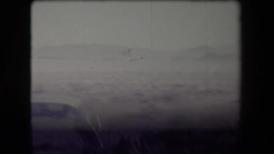 Partial view from near a car looking across a hazy Arizona desert landscape toward low mountains, with dark film border at the frame edge.