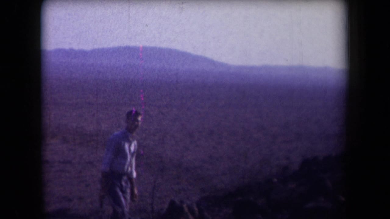 1958 Arizona 8mm frame showing an adult man crossing open desert terrain with mountains in the distance and a purple color cast.