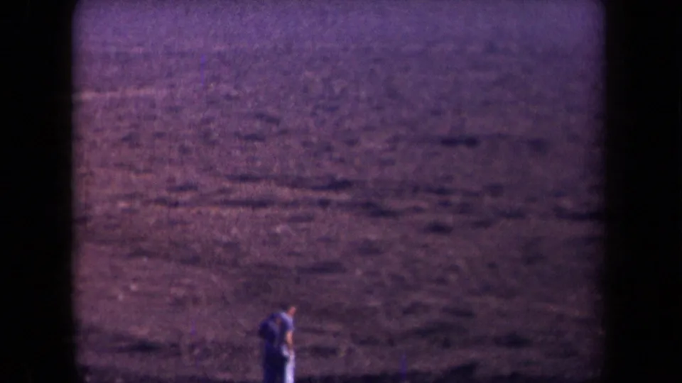1958 Arizona 8mm frame with a small adult figure near the lower edge of a broad, grainy desert view.