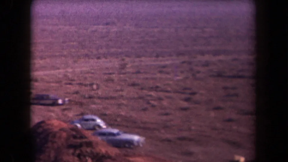 1958 Arizona 8mm frame showing parked cars beside a dirt road in a broad, dry desert landscape.