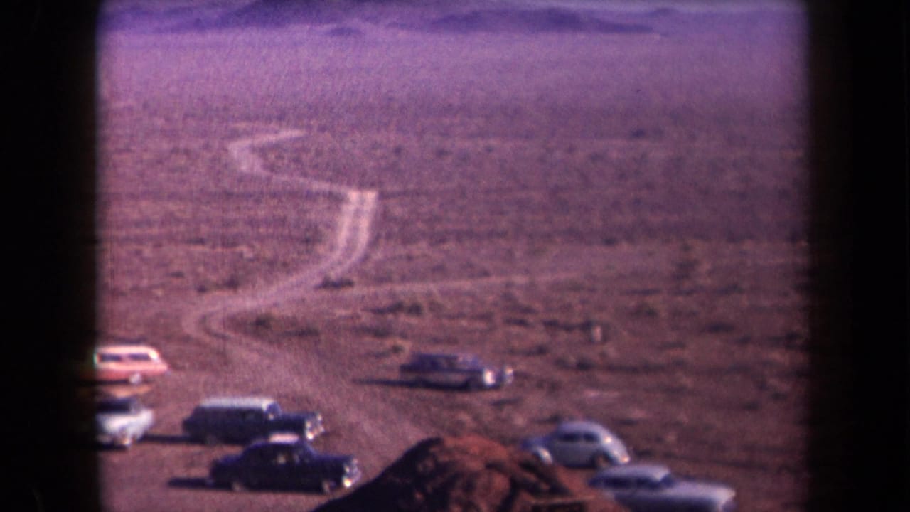 1958 Arizona desert scene with classic cars parked near a winding unpaved road and distant low mountains.