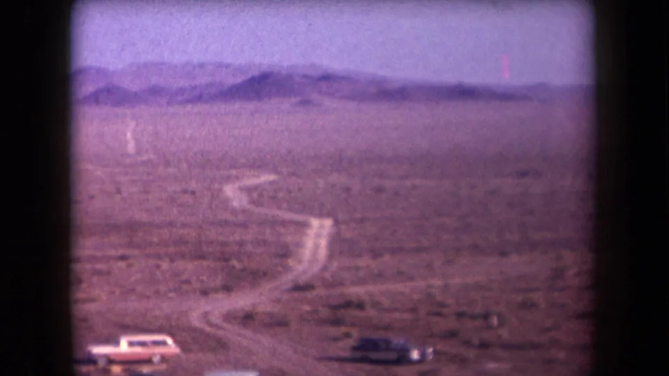 Soft 8mm view of an Arizona desert road curving past parked cars toward distant mountains.