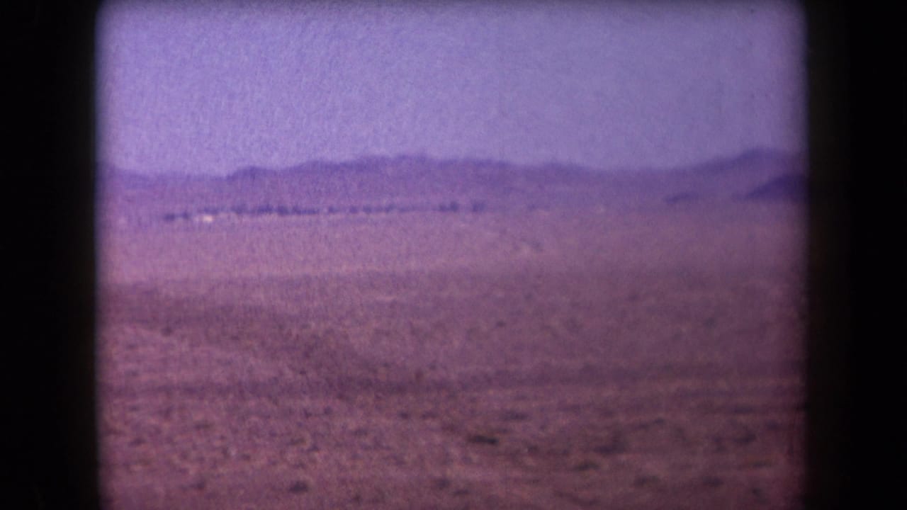 1958 Arizona home-movie frame showing an open desert plain, low mountains on the horizon, and soft faded 8mm color.