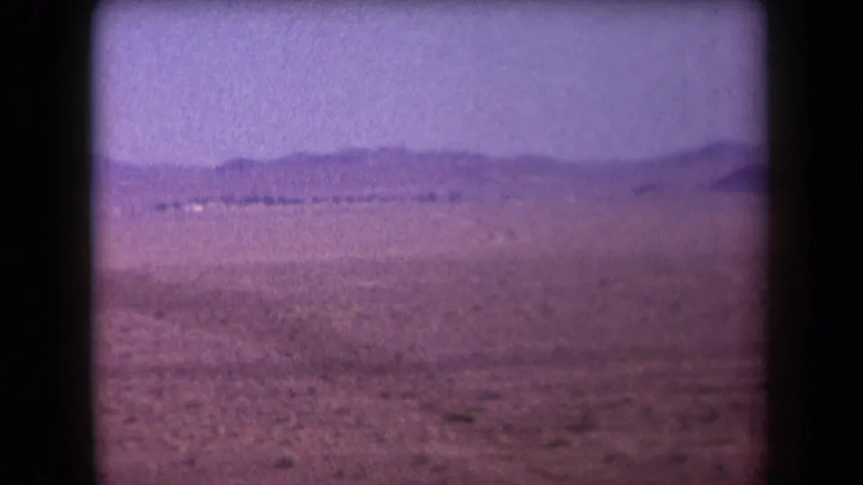 1958 Arizona home-movie frame showing an open desert plain, low mountains on the horizon, and soft faded 8mm color.