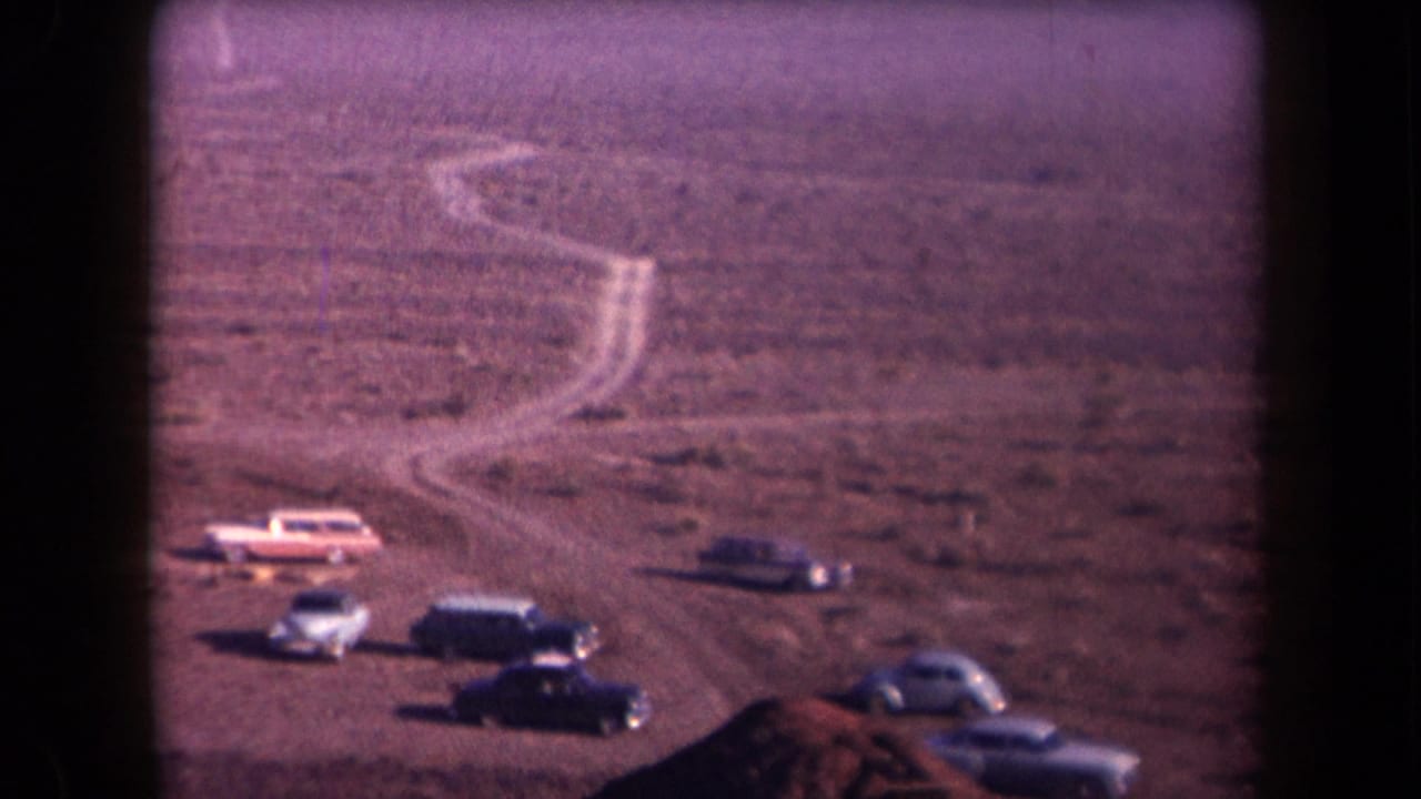 Several vintage cars parked near a winding dirt path in desert terrain.