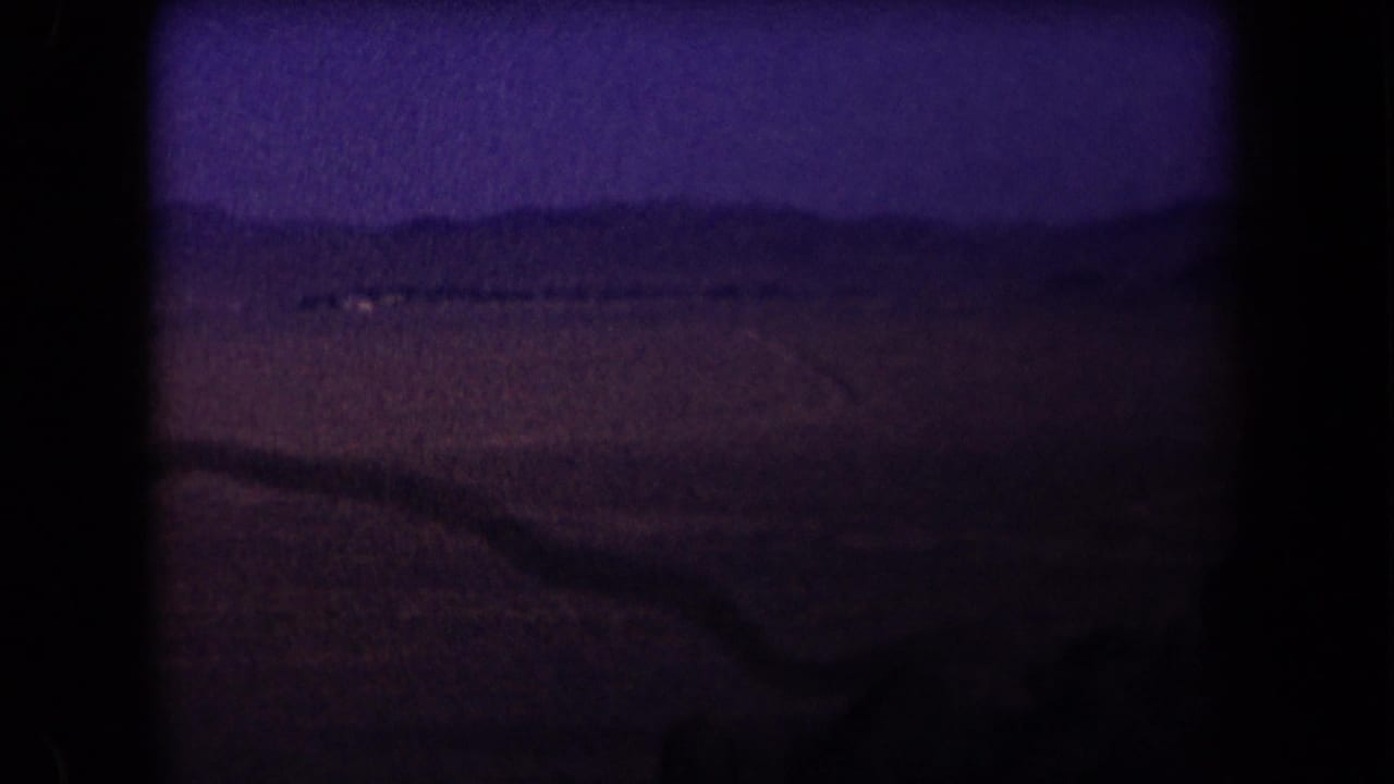 Dark desert landscape with a faint road line, distant low hills, and blue-purple night sky.