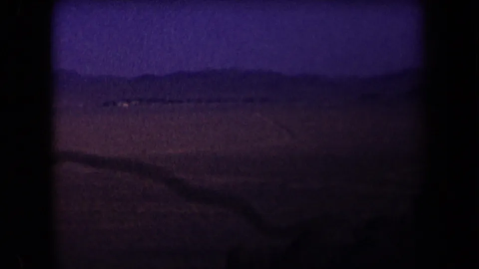 1958 Arizona 8mm frame showing a dim desert road or wash line leading toward low hills under a blue-purple night sky.