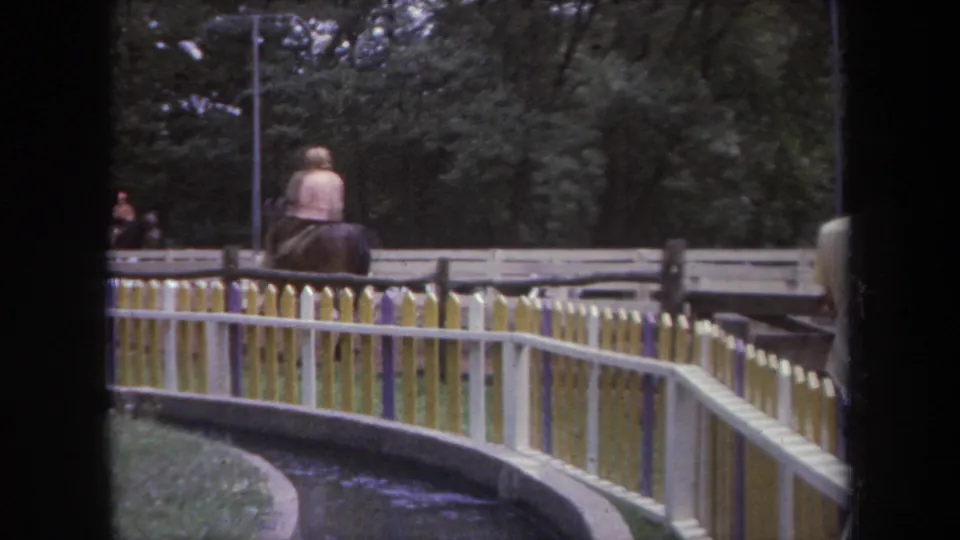 1968 Michigan frame showing a horseback rider from behind on the fenced track, with trees and a water channel nearby.
