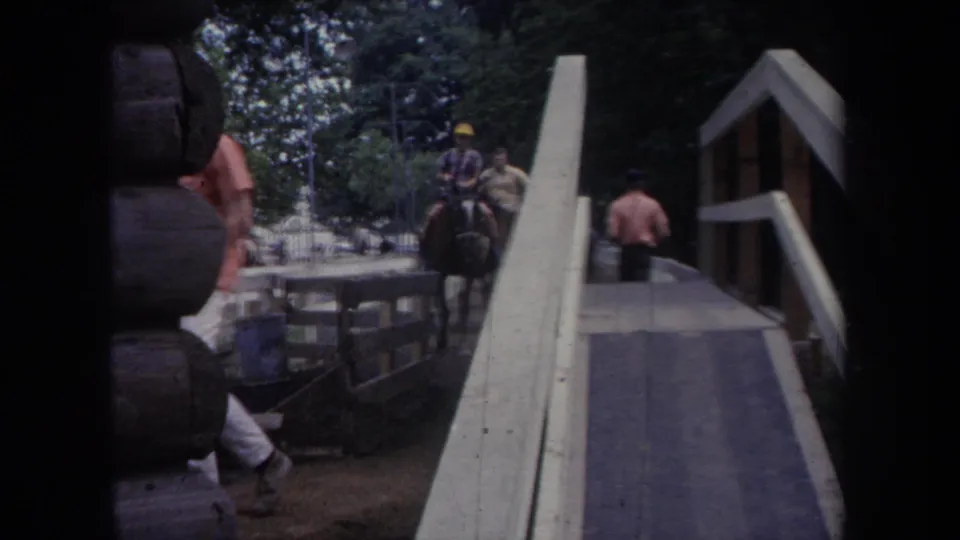 1968 Michigan 8mm frame showing a man near a wooden bridge while a rider in a yellow hat approaches on horseback.