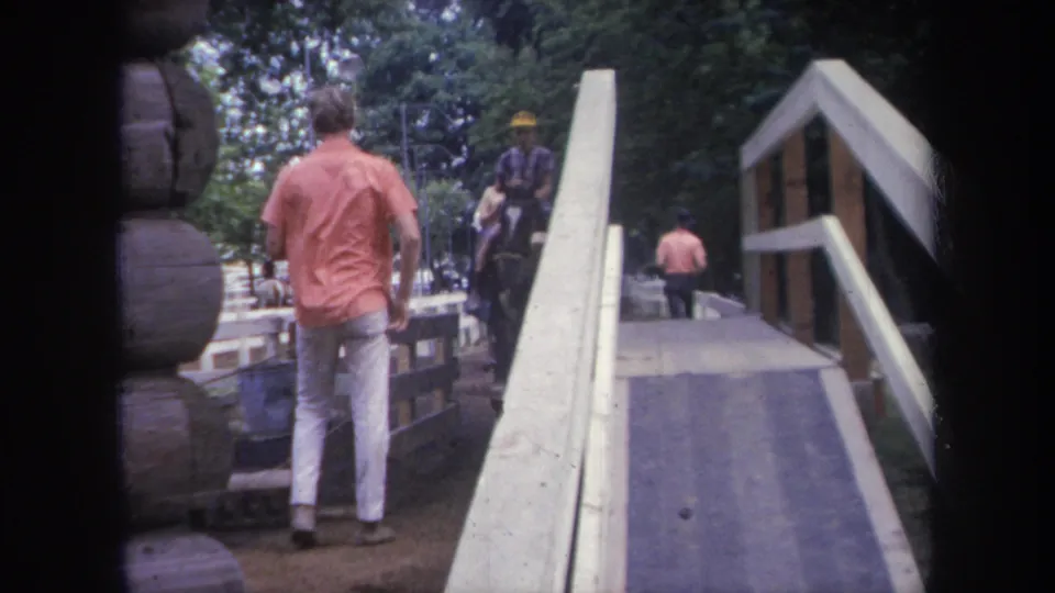1968 Michigan 8mm frame showing a man in a pink shirt and white pants approaching a bridge near a mounted rider.
