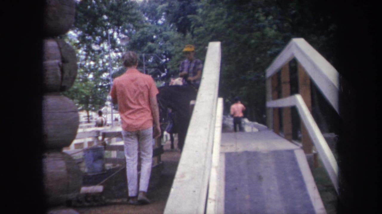 1968 Michigan 8mm frame showing a man in a pink shirt walking beside a horse with a rider in a yellow hat near a wooden ramp.