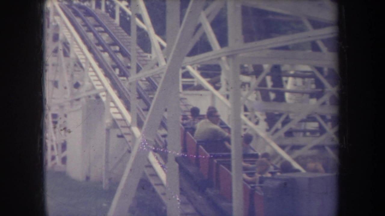 Wooden roller coaster cars move through a white-painted structure with seated riders visible.