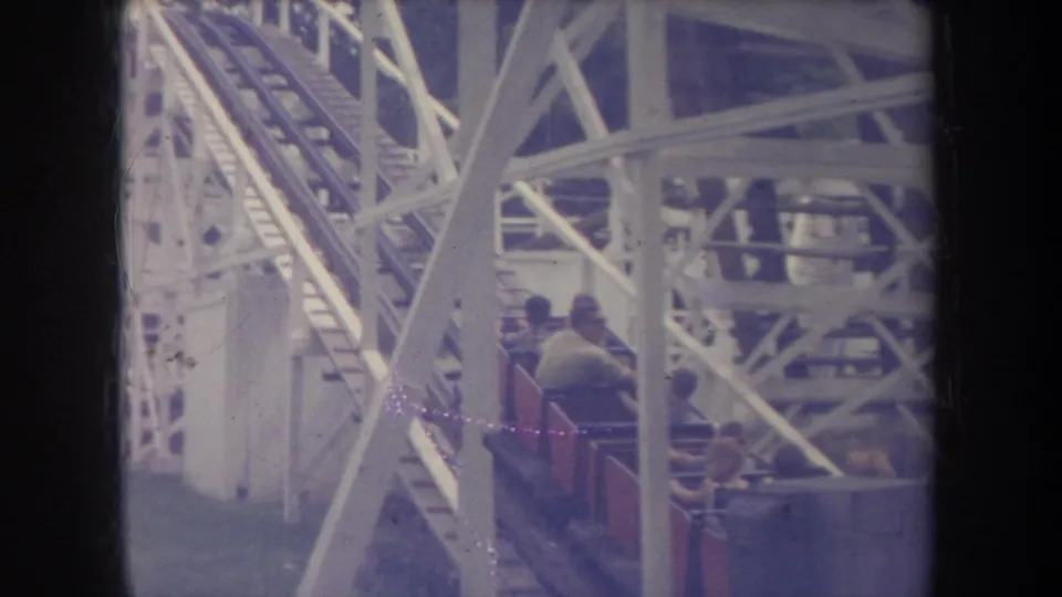 1968 Michigan 8mm frame showing riders in red roller coaster cars amid a white wooden coaster structure.