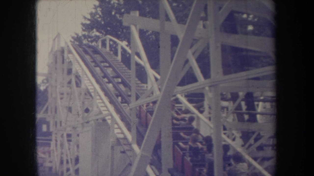 Roller coaster track and support beams fill the frame as riders pass behind the structure.