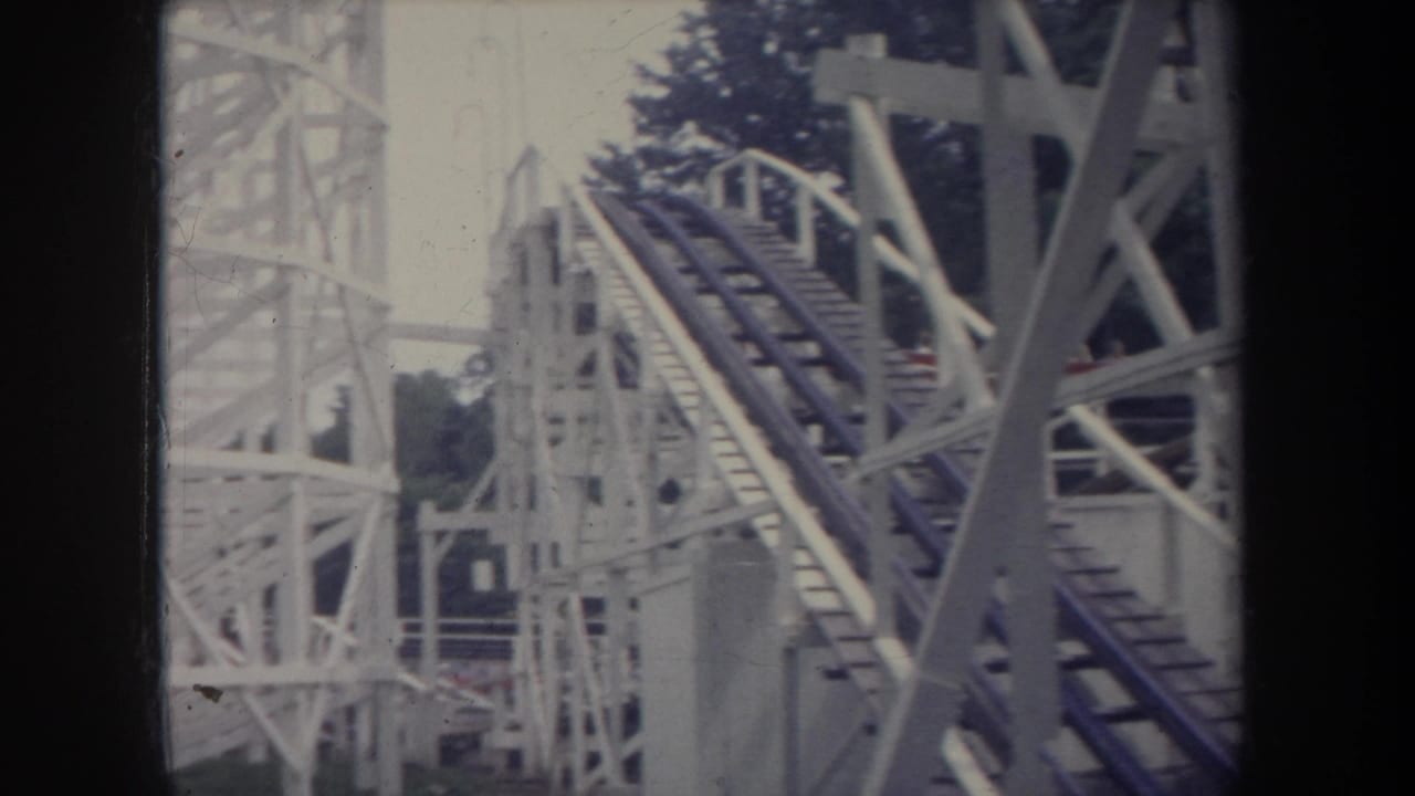 White wooden roller coaster lift hill with dark tracks and trees behind it.