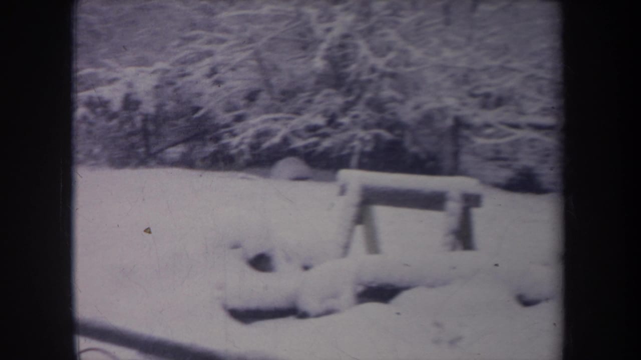 1968 Michigan home-movie frame showing a snowy backyard, wooden bench, bare trees, and dark 8mm film borders.