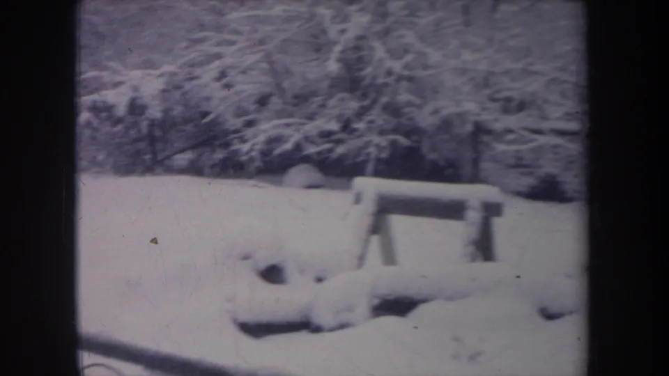 1968 Michigan home-movie frame showing a snowy backyard, wooden bench, bare trees, and dark 8mm film borders.