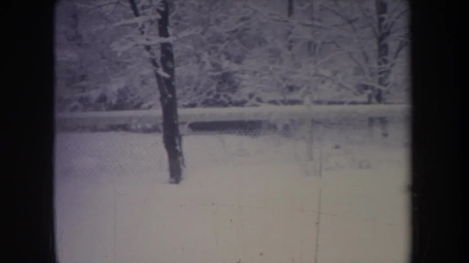 1968 Michigan 8mm frame showing a snow-covered residential yard through dark window mullions, with bare trees and a chain-link fence.