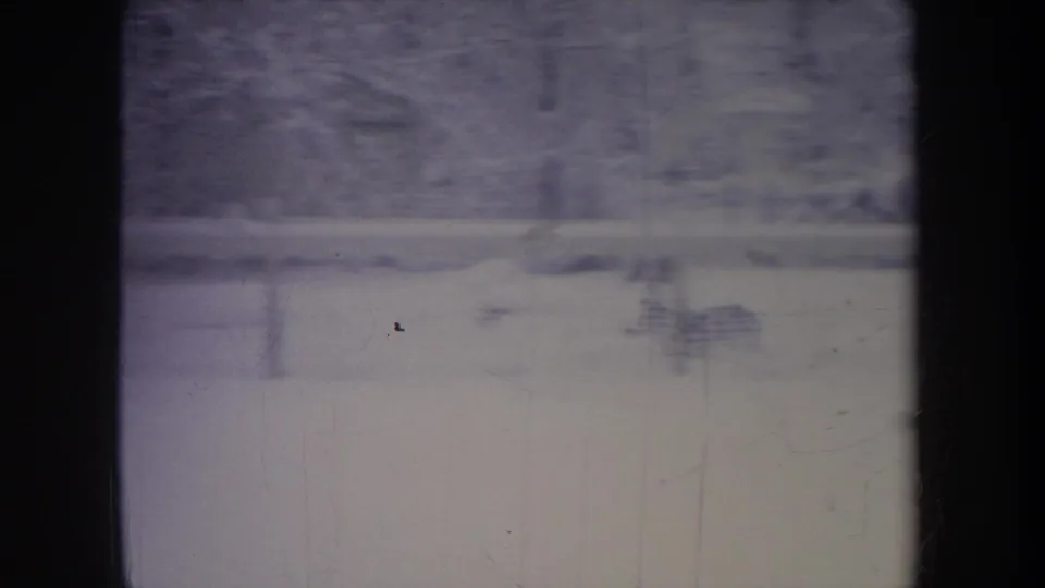 Faded 8mm view of a Michigan winter backyard in 1968, showing snow, distant trees, and dark window framing.