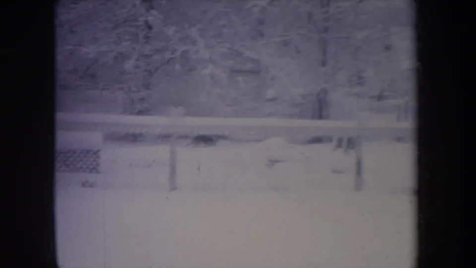 Faded 8mm frame of a 1968 Michigan backyard with snow, fencing, bare trees, and foreground window bars.