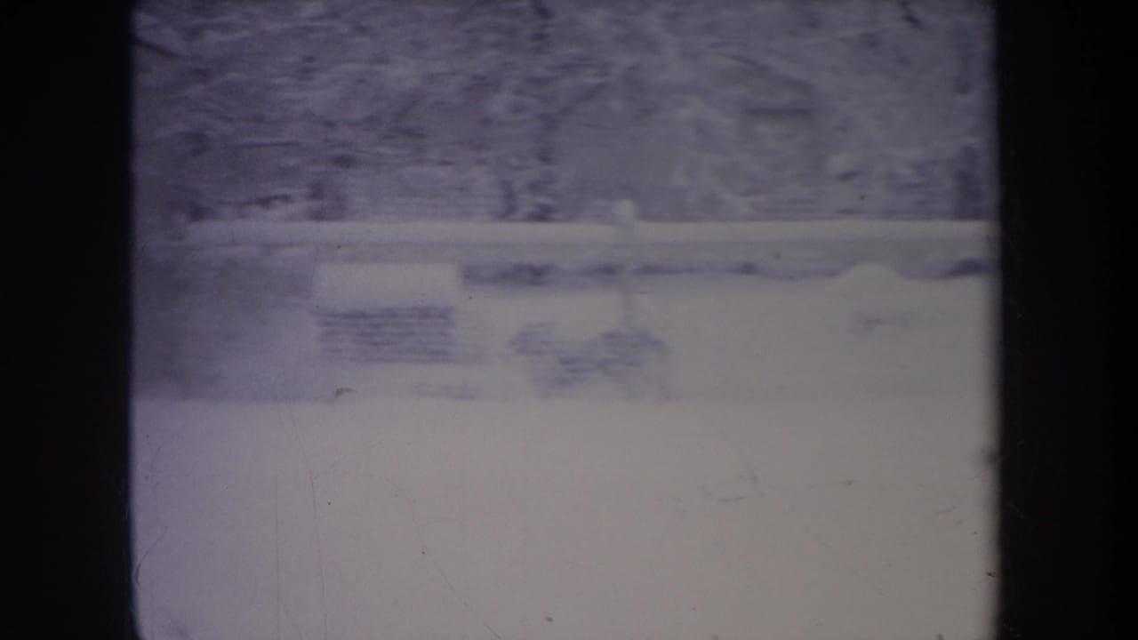 1968 Michigan 8mm frame showing a snowy yard, small house, fence line, bare trees, and heavy frame-edge shadowing.