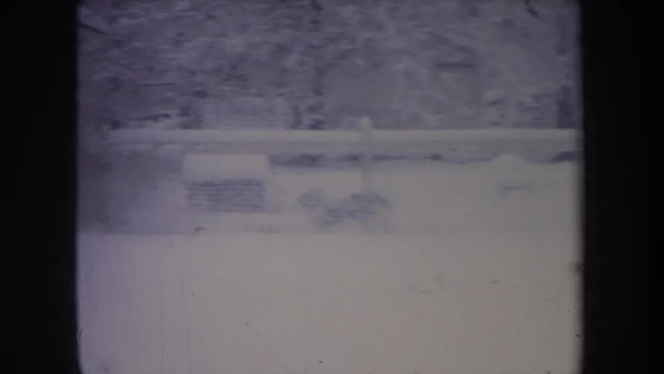 1968 Michigan 8mm frame showing a snowy yard, small house, fence line, bare trees, and heavy frame-edge shadowing.