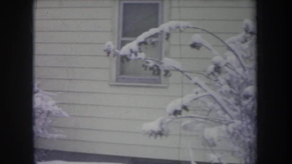 1968 Michigan home-movie view of a house exterior with snow-heavy branches and a small window.