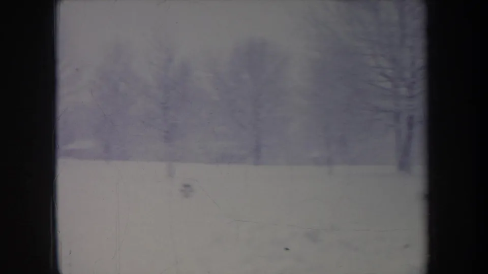 1968 Michigan home-movie frame showing a snowy open area and bare trees, with soft focus and blue-purple film fading.
