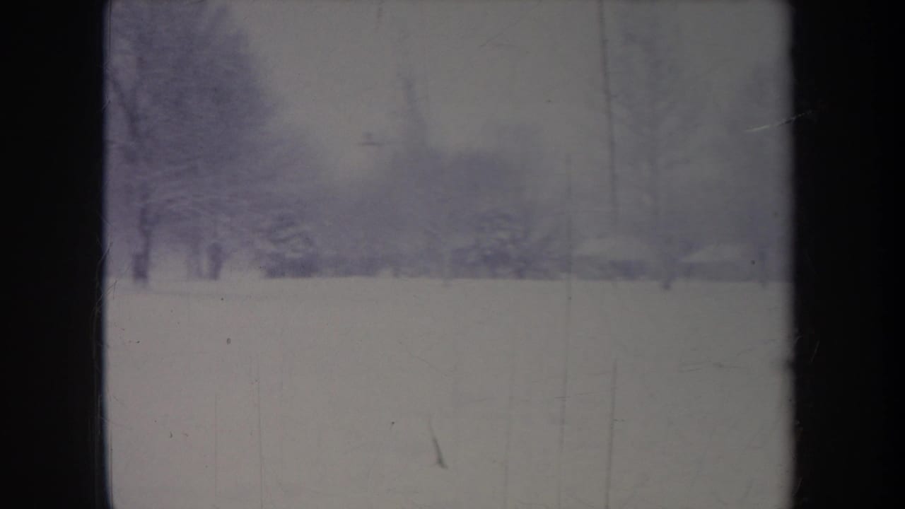 1968 Michigan winter frame with snow-covered ground, bare trees, and a distant building partly obscured by haze and film fading.