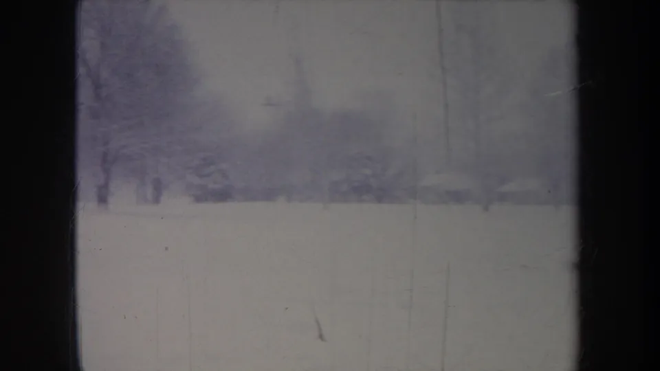 1968 Michigan winter frame with snow-covered ground, bare trees, and a distant building partly obscured by haze and film fading.