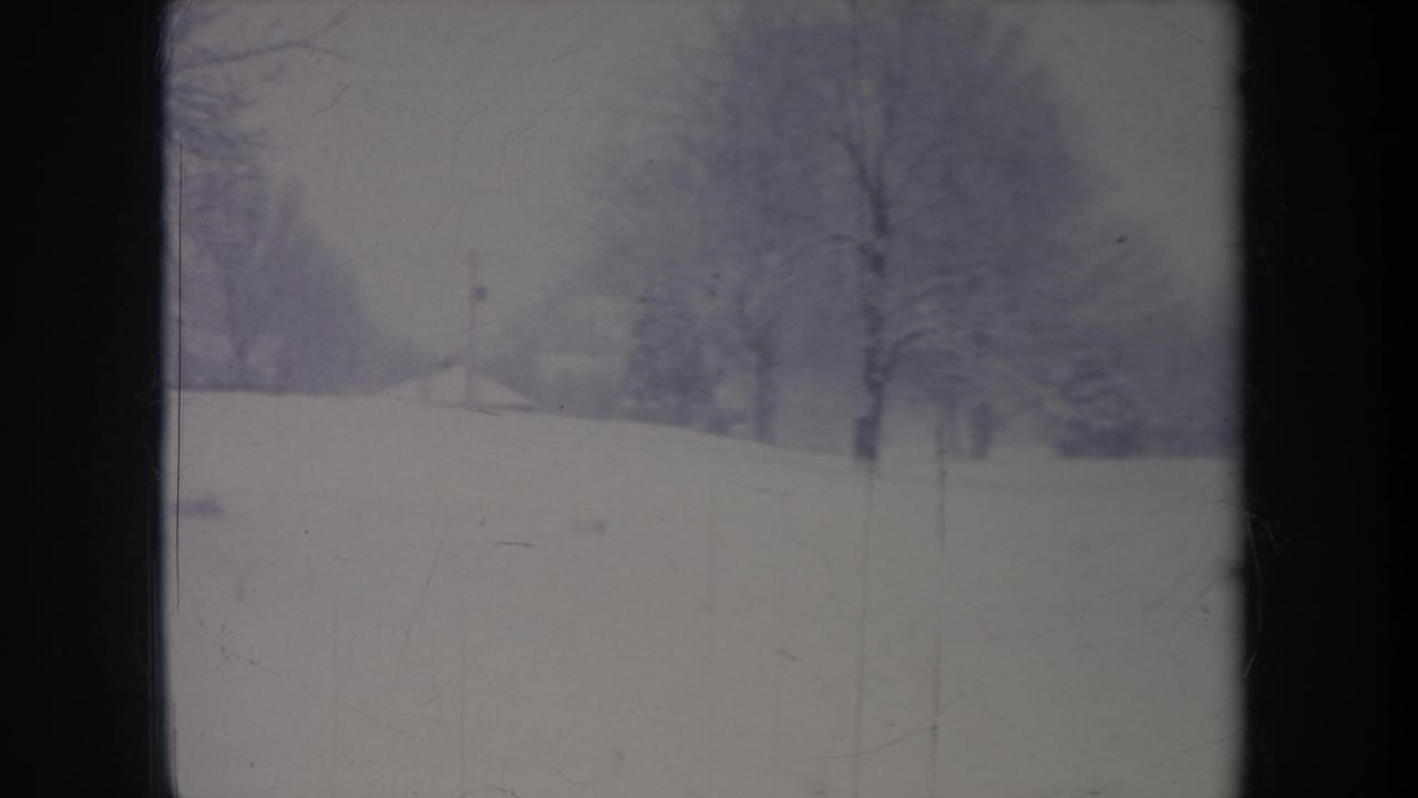 1968 Michigan 8mm frame showing a snowy field and bare trees, framed by dark vertical bands from the camera position or film edge.