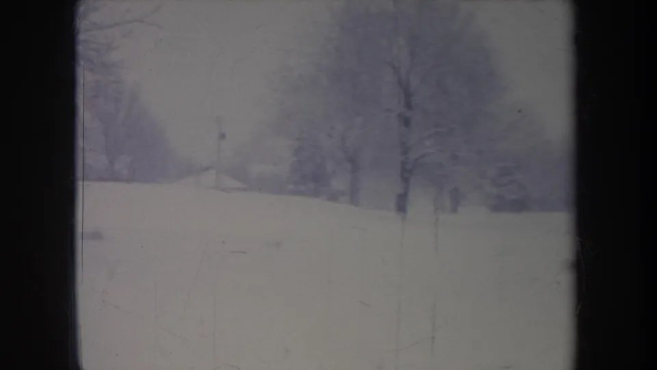 1968 Michigan 8mm frame showing a snowy field and bare trees, framed by dark vertical bands from the camera position or film edge.