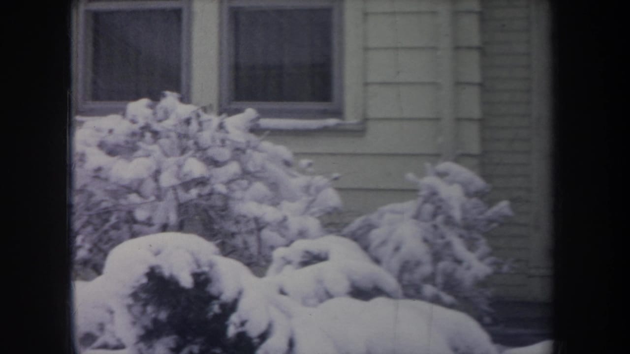1968 Michigan winter frame showing snow-packed shrubs below rectangular house windows, with pale siding and soft 8mm color fading.