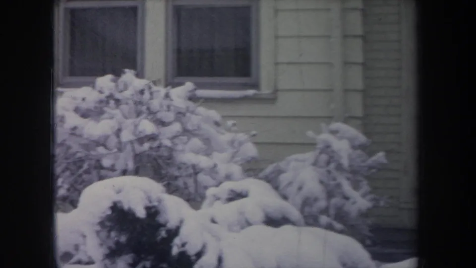 1968 Michigan winter frame showing snow-packed shrubs below rectangular house windows, with pale siding and soft 8mm color fading.