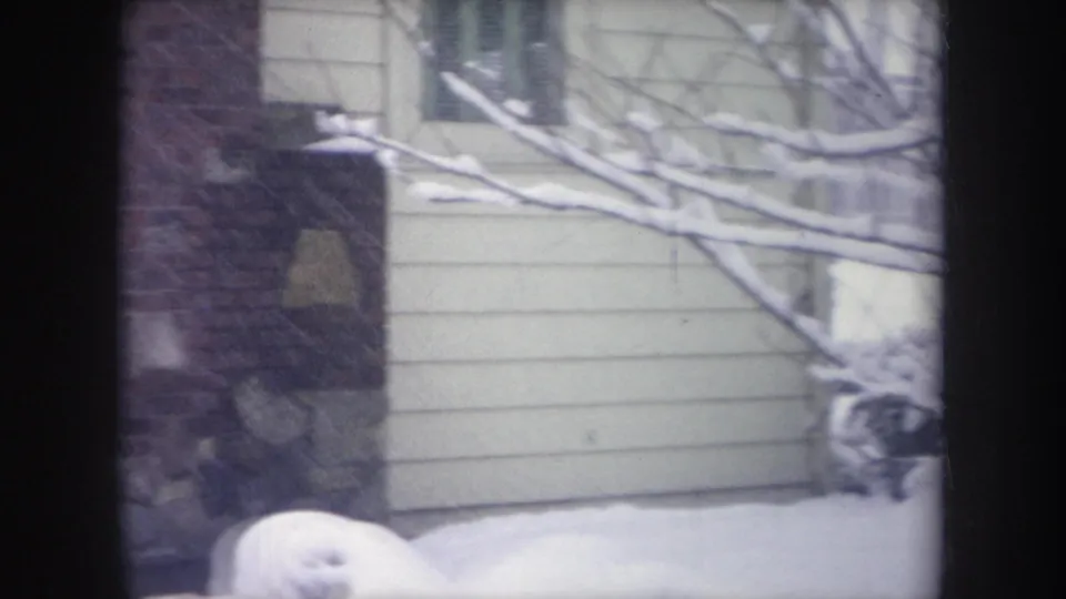 1968 Michigan home-movie frame with snow on branches and yard beside a white-sided house and brick exterior section.