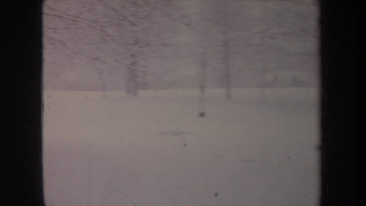 Faded 8mm frame of a snow-covered Michigan setting in 1968, with bare trees and dark foreground bars.