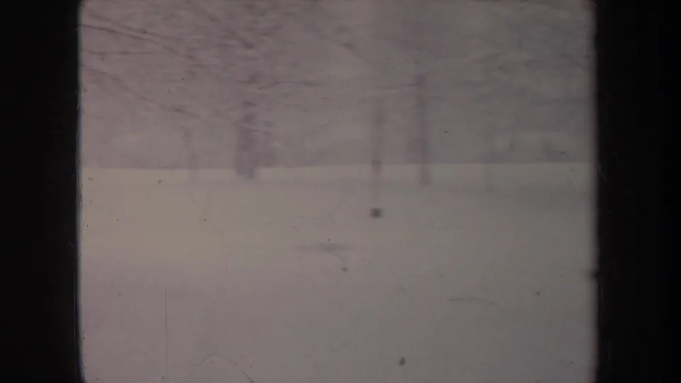 Faded 8mm frame of a snow-covered Michigan setting in 1968, with bare trees and dark foreground bars.